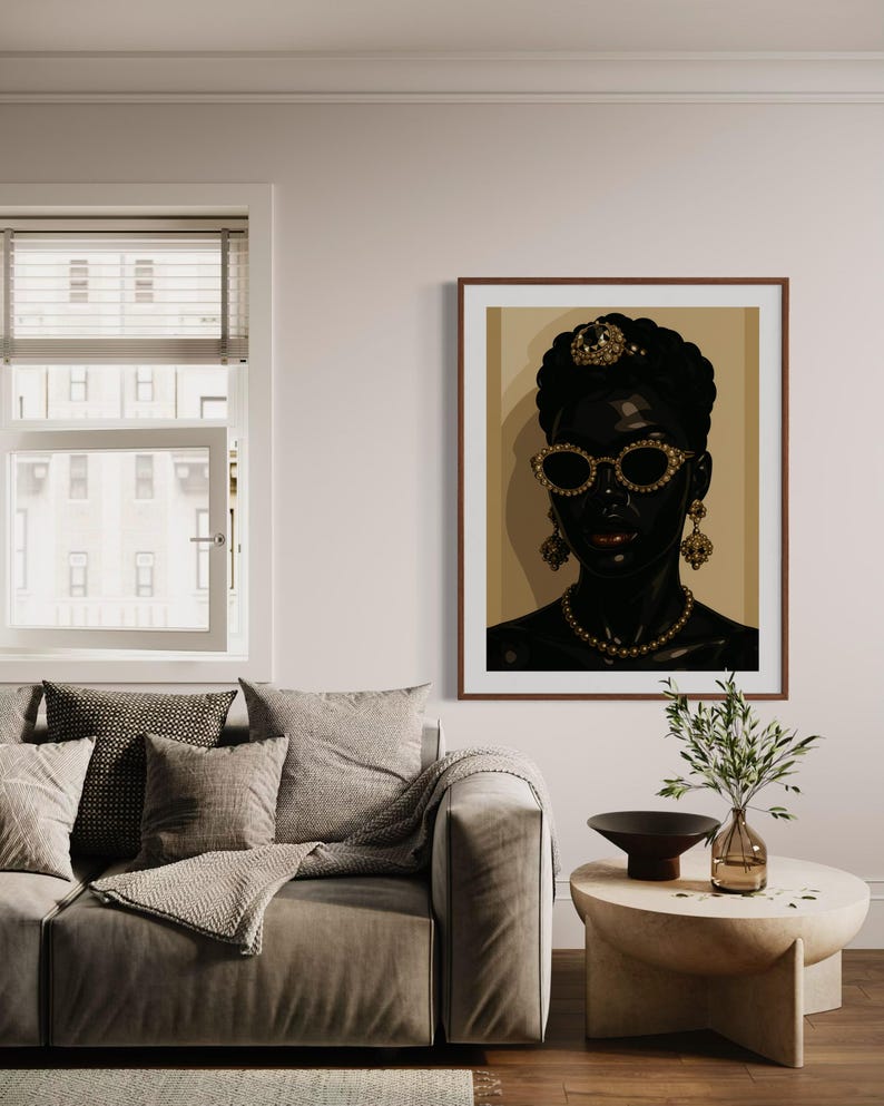 May include: A framed portrait of a person with dark skin, wearing gold-rimmed sunglasses, a jeweled headpiece, and earrings. The portrait is displayed in a living room setting with a sofa, pillows, and a side table.