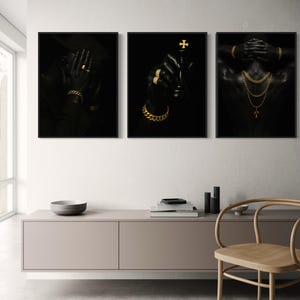 May include: Set of three framed art prints featuring black and gold imagery. One print shows a person wearing a hat and gold jewelry, another holds a chess piece, and the third displays a person with gold necklaces and bracelets.