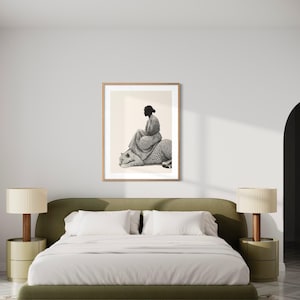 May include: A framed black and white art print depicts a person seated on a leopard. The artwork is displayed above a green bed with white bedding, flanked by matching bedside tables and lamps. The room has a neutral color palette.