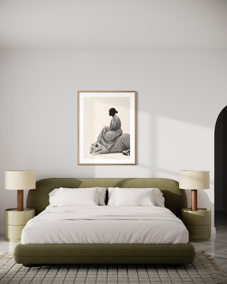 May include: A framed black and white art print depicts a person seated on a leopard. The artwork is displayed above a green bed with white bedding, flanked by matching bedside tables and lamps. The room has a neutral color palette.
