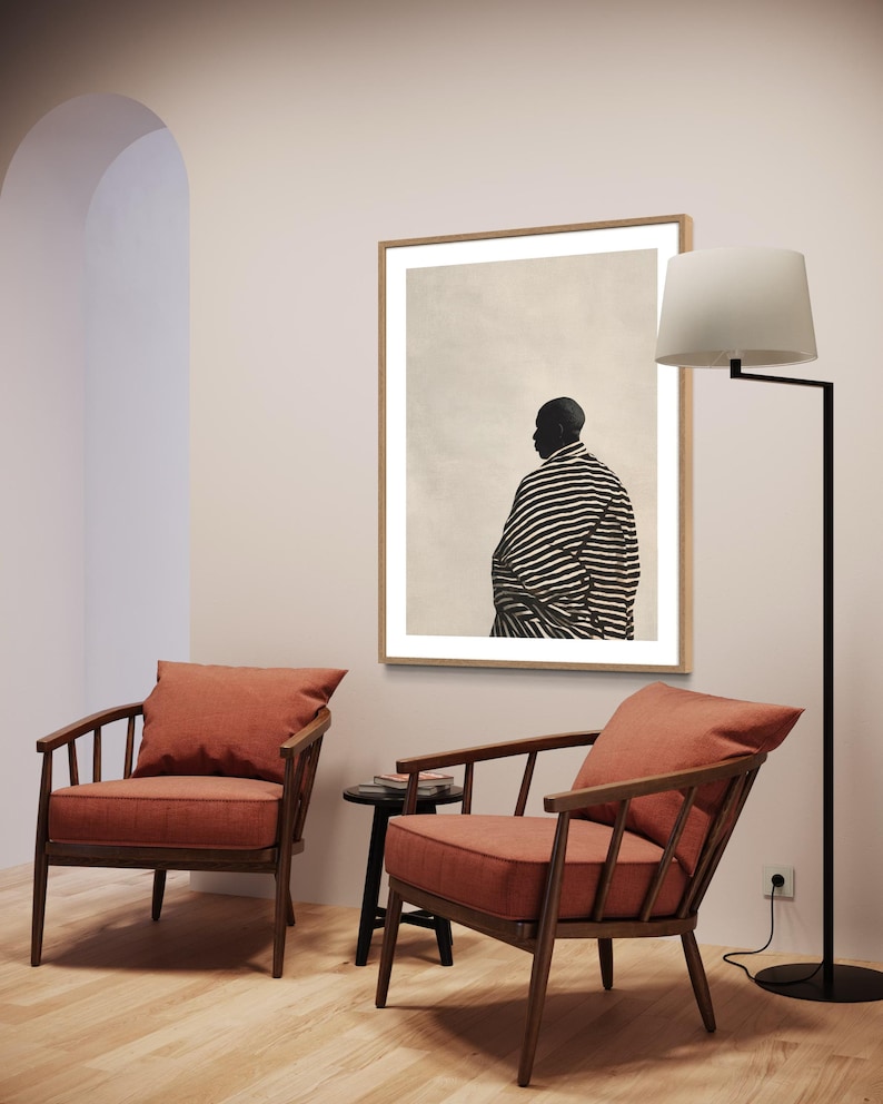 May include: A room interior with two wooden armchairs with terracotta cushions, a framed artwork with a figure in black and white stripes, and a black floor lamp. The walls are light-coloured and the floor is wooden.