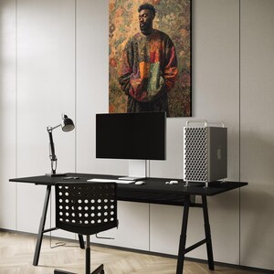 K&ouml;nnte beinhalten: Ein modernes B&uuml;ro mit einem schwarzen Schreibtisch, Stuhl und Monitor. Ein gro&szlig;es gerahmtes Kunstwerk mit einem Portr&auml;t einer Person in einem bunten Pullover h&auml;ngt an der Wand. Ein silberner Computer-Tower und eine schwarze Schreibtischlampe sind ebenfalls zu sehen.