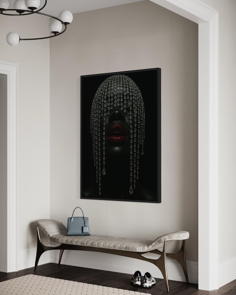 Pode incluir: Uma impress&atilde;o de arte emoldurada com um retrato de uma pessoa com pele escura, adornada com um adorno de cabe&ccedil;a com joias e l&aacute;bios vermelhos. A obra de arte est&aacute; pendurada acima de um banco com uma bolsa azul e t&ecirc;nis.