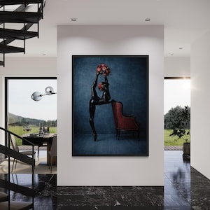 May include: A framed art print showing a black sculpture of a person in a ballet pose, holding a bouquet of red flowers. The sculpture is set against a blue textured backdrop, with a red armchair nearby.