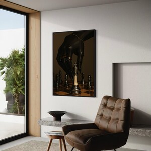 Op de afbeelding: Een ingelijst kunstwerk dat een zwarte hand met gouden sieraden afbeeldt die een schaakstuk verplaatst. De schaakstukken staan op een schaakbord. Het kunstwerk wordt getoond in een moderne kamer met een bruine leren stoel en een kleine houten kruk.