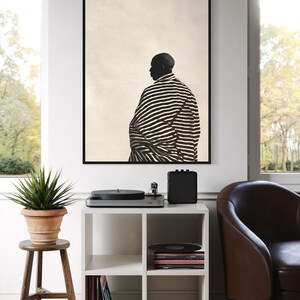 May include: A monochrome art print shows a person in profile, wearing a striped robe. The artwork is above a white cube shelf with vinyl records and a record player. A potted plant sits on a wooden stool, next to a window.