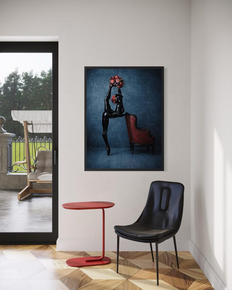 May include: A framed art print showing a black sculpture of a dancer with a bouquet of red flowers, next to a red armchair. A red side table and a black chair are in the foreground. The room has a hardwood floor and a large window.