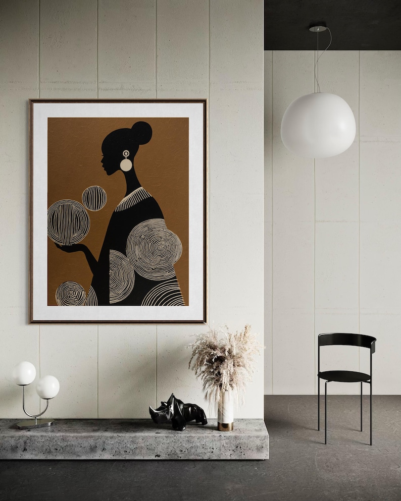 May include: A framed art print featuring a black and white silhouette of a woman holding circular designs. The artwork is set against a brown background with a white border. The print is displayed in a modern interior setting.