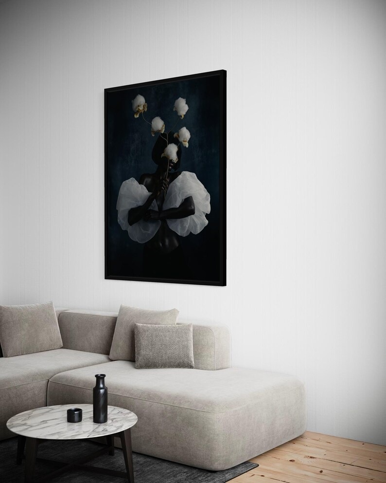 May include: A framed art print featuring a person with white flowers and a white ruffled garment against a dark blue background. The artwork is displayed above a light gray sectional sofa and a marble-topped coffee table.