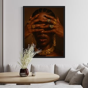 K&ouml;nnte beinhalten: Ein Portr&auml;t einer Person mit dunkler Haut, die eine goldene Kettenkette und mehrere goldene Ringe an den Fingern tr&auml;gt. Ihre Augen sind von ihren H&auml;nden bedeckt und sie tr&auml;gt goldene Ohrringe.