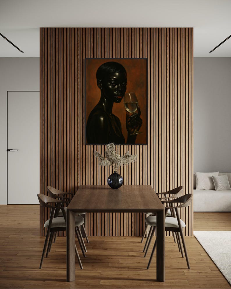 May include: A framed portrait of a person holding a glass of wine, with a dark complexion and red lipstick. The artwork hangs on a wooden slatted wall, above a wooden dining table with four chairs. A vase with decorative branches sits on the table.