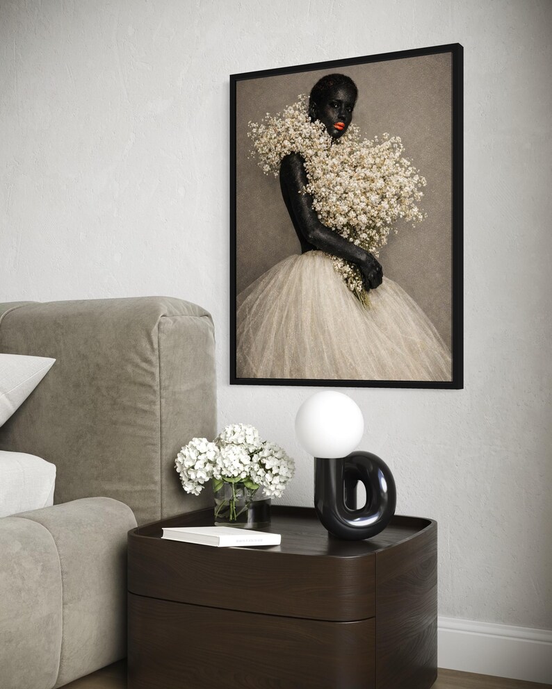 May include: A framed wall art print featuring a person with dark skin and bright orange lips, wearing a voluminous white tulle skirt and holding a large bouquet of white baby's breath flowers against a neutral gray background.