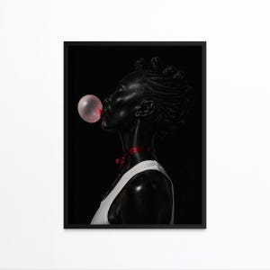 May include: A framed art print featuring a profile of a person blowing a pink bubble. The person is wearing a white tank top and a red ribbon around their neck. The background is black.