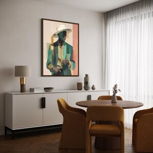 May include: A framed art print depicts a man in a hat and suit, holding a glass. The artwork features a color palette of teal, beige, and peach. The print hangs above a white cabinet, with a round wooden table and mustard-colored chairs in the foreground.