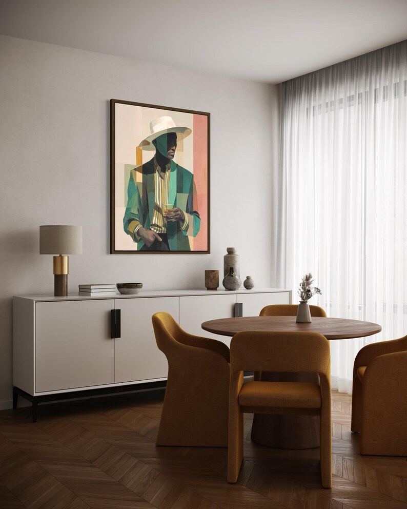 May include: A framed art print depicts a man in a hat and suit, holding a glass. The artwork features a color palette of teal, beige, and peach. The print hangs above a white cabinet, with a round wooden table and mustard-colored chairs in the foreground.