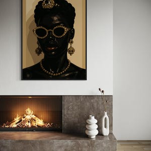 May include: A framed art print featuring a stylized portrait of a person with dark skin. The person wears gold-rimmed sunglasses, a jeweled headpiece, earrings, and a necklace. The artwork is set against a neutral background.