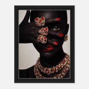 Puede incluir: Impresión enmarcada de una persona con piel oscura adornada con joyas de oro y piedras preciosas rojas. La mano cubre parte de la cara, mostrando anillos, pendientes y un collar. Esmalte de uñas y lápiz labial rojos completan el look.