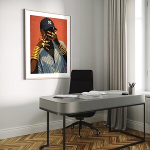 May include: Framed art print featuring a person wearing a navy blue baseball cap with a white "NY" logo, gold jewelry, and a blue and white striped shirt. The artwork is displayed in a modern office setting with a gray desk and black chair.