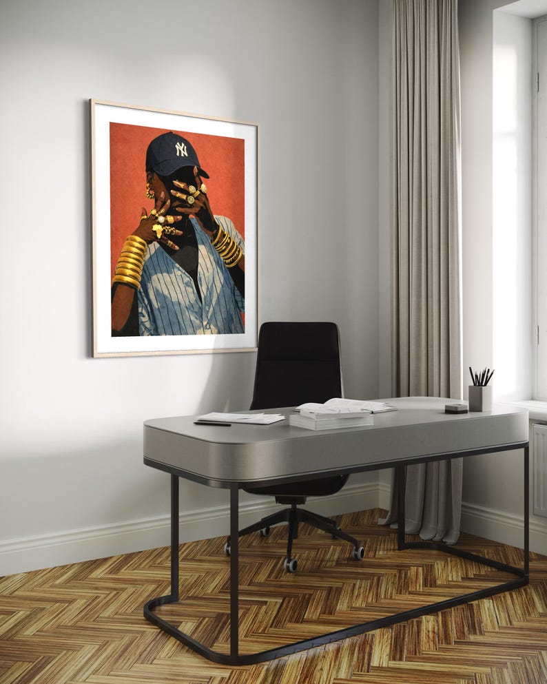 May include: Framed art print featuring a person wearing a navy blue baseball cap with a white "NY" logo, gold jewelry, and a blue and white striped shirt. The artwork is displayed in a modern office setting with a gray desk and black chair.