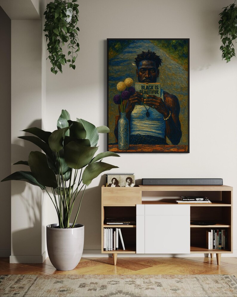 Puede incluir: Una obra de arte enmarcada representa a una persona sosteniendo un libro con el texto "BLACK IS BEAUTIFUL". La obra de arte cuelga sobre un mueble de madera con una puerta blanca. Tambi&eacute;n se ven una gran planta en maceta y plantas colgantes.