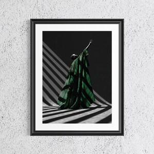 May include: Framed art print featuring a person in a flowing green and black striped garment, with an arm raised. The figure is positioned in a room with dramatic light and shadow from a window.