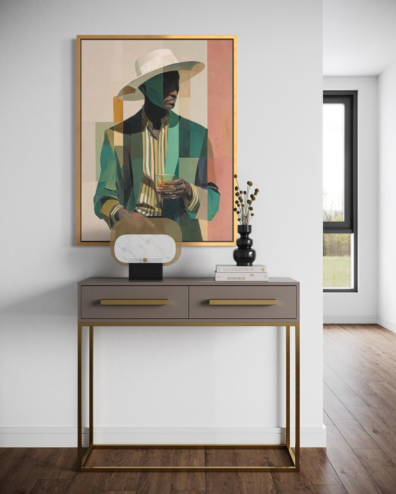May include: An abstract painting of a person in a hat and suit, with green and beige tones, hangs above a gray console table with gold accents. A decorative object with a marble top and a black vase with dried flowers sit on the table. The room has hardwood floors.