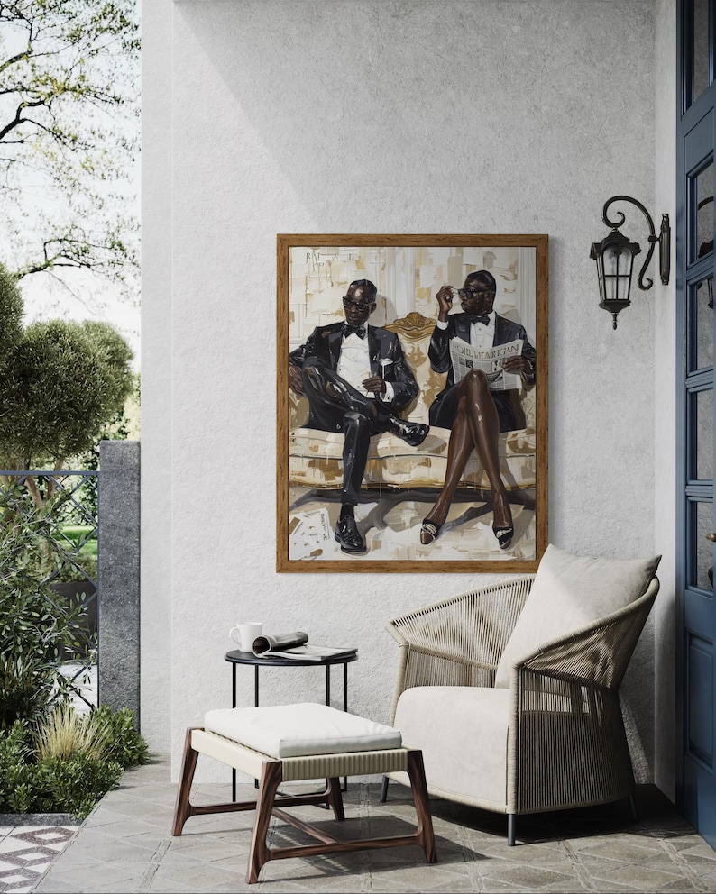 May include: An oil painting in a wooden frame depicts two figures in tuxedos seated on a sofa. The artwork hangs above a woven chair and ottoman on a patio. A small table holds a mug and rolled newspaper.