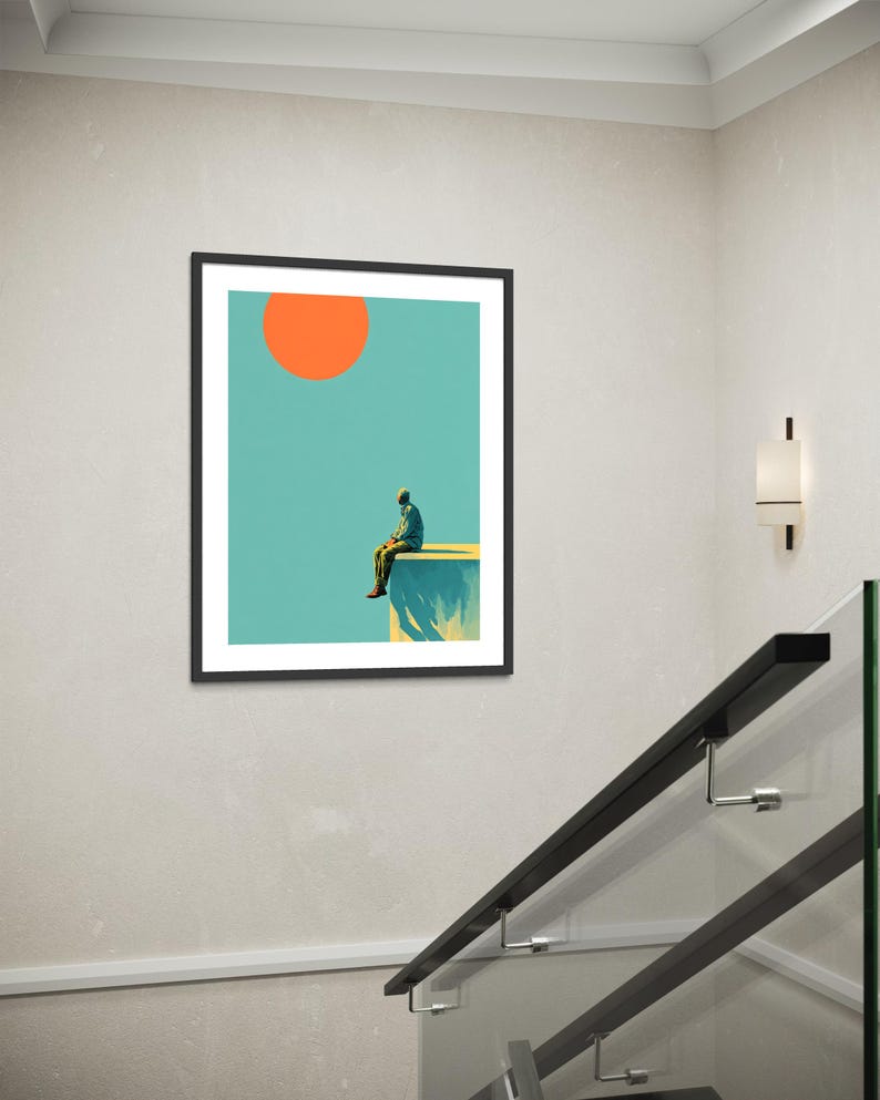 May include: Framed art print featuring a minimalist illustration. A person sits on the edge of a cliff, with a large orange sun in a teal sky. The artwork is in a black frame, suitable for home decor.