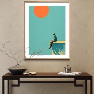 May include: A framed art print featuring a surreal landscape. A figure sits on a ledge under a bright orange sun against a teal sky. The artwork has a minimalist style with a gold frame, suitable for home decor.