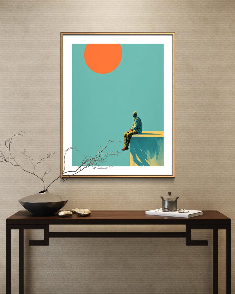 May include: A framed art print featuring a surreal landscape. A figure sits on a ledge under a bright orange sun against a teal sky. The artwork has a minimalist style with a gold frame, suitable for home decor.