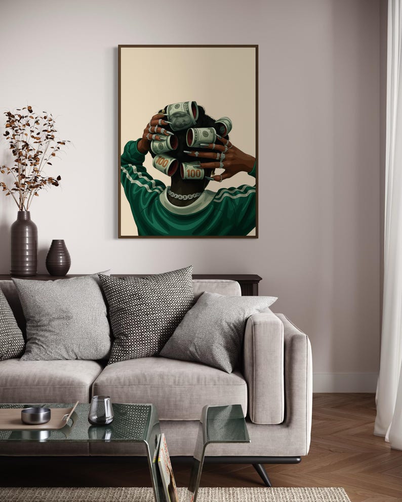 May include: A framed art print depicts a person with dollar bills rolled into curlers. The person wears a green and white striped shirt and a silver chain. The artwork is displayed above a gray sofa with decorative pillows.
