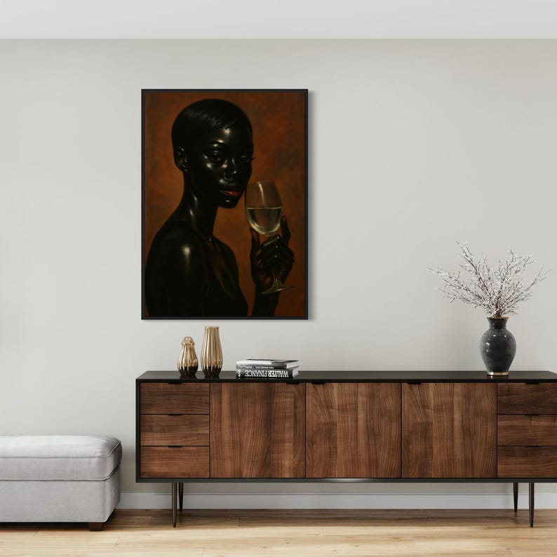 May include: A framed art print featuring a dark-skinned person holding a glass of white wine. The artwork has a warm, brown background and is displayed above a wooden cabinet with decorative items.