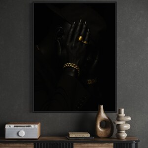 May include: A framed black and white portrait of a person with their hand covering their face. The person is wearing gold jewelry, including a ring and a bracelet. The image is dark and moody, with a focus on the person's features and accessories.