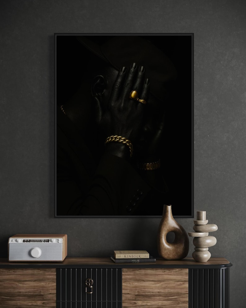 May include: A framed black and white portrait of a person with their hand covering their face. The person is wearing gold jewelry, including a ring and a bracelet. The image is dark and moody, with a focus on the person's features and accessories.