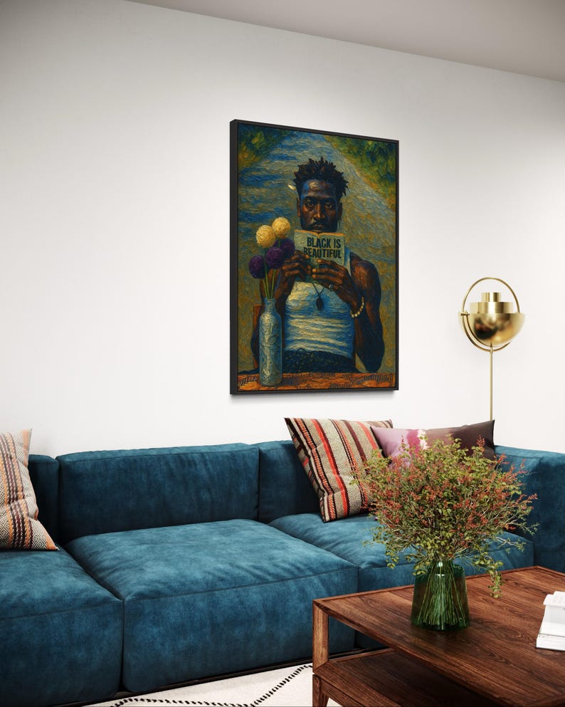 Puede incluir: Una obra de arte enmarcada representa a una persona sosteniendo un libro con el texto "BLACK IS BEAUTIFUL". La obra de arte se exhibe sobre un sof&aacute; azul con cojines decorativos. Un jarr&oacute;n con flores est&aacute; cerca de la obra de arte, y una mesa de centro de madera est&aacute; frente al sof&aacute;.