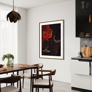 May include: A framed art print depicts a person holding a glass of red liquid, wearing a gold chain. The artwork hangs in a modern dining room with a wooden table and chairs. A black pendant light hangs above the table.