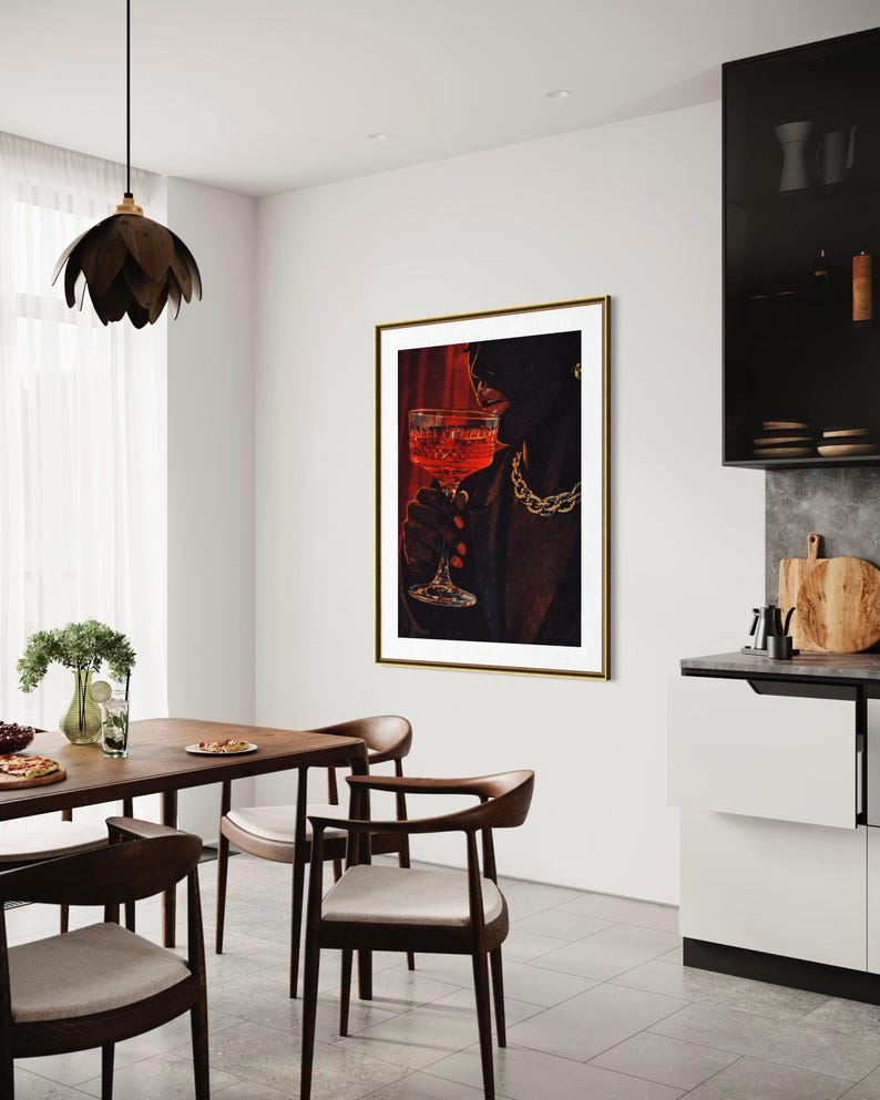 May include: A framed art print depicts a person holding a glass of red liquid, wearing a gold chain. The artwork hangs in a modern dining room with a wooden table and chairs. A black pendant light hangs above the table.