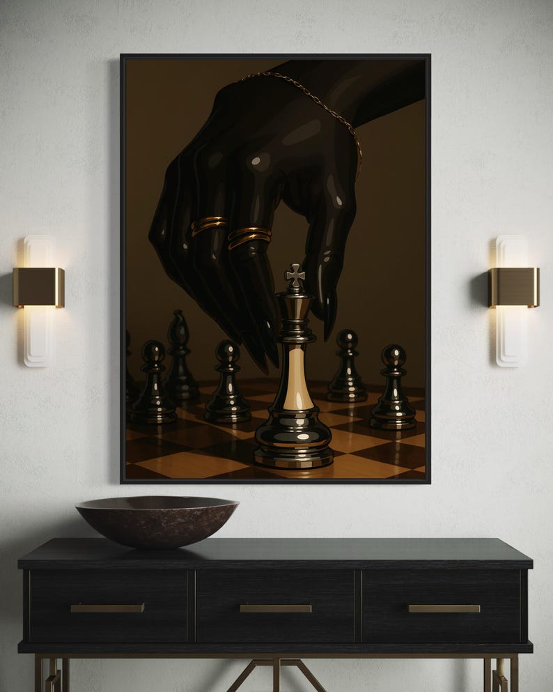 Op de afbeelding: Een ingelijste kunstdruk toont een zwarte hand met gouden ringen en een armband, boven een schaakbord. De koning schaakstuk staat centraal. Het kunstwerk wordt weergegeven boven een donkere houten console.