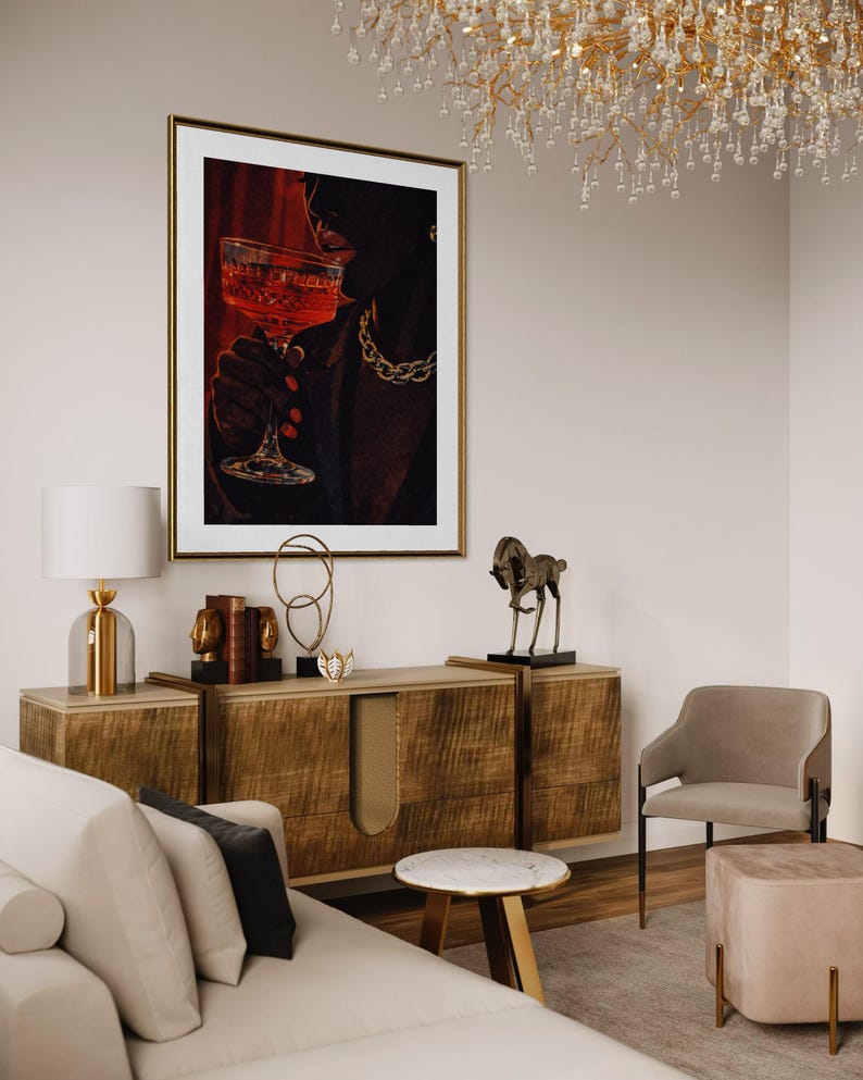 May include: An interior design scene featuring a framed artwork of a person holding a cocktail glass. The artwork is above a wooden cabinet with decorative items. A sofa, chair, and side table complete the room's decor. A chandelier hangs from the ceiling.