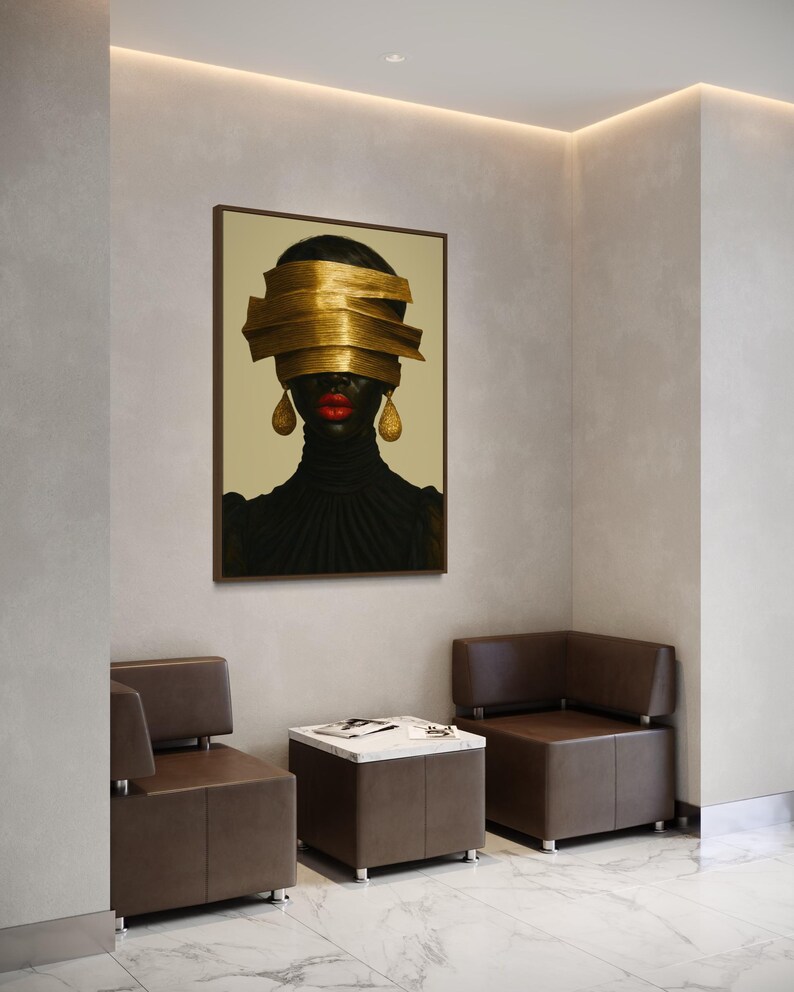 May include: An artistic portrait of a person with dark skin, red lips, and gold earrings. The person's eyes are covered by layered gold bands. The portrait is in a brown frame, hanging above two brown leather chairs and a marble-topped table.