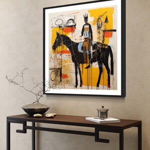 May include: Abstract art print depicting a black horse and rider, set against a backdrop of yellow, orange, and white brushstrokes. The artwork is framed in a black frame and displayed on a wall.
