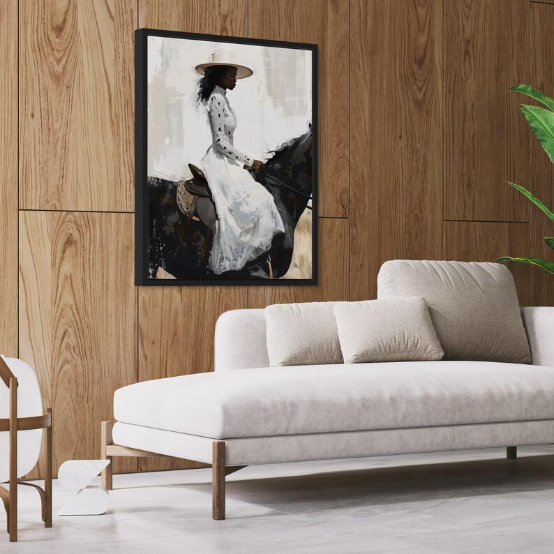 May include: A framed art print shows a person on horseback. The person wears a white dress and hat. The artwork is in a black frame, mounted on a wood-panelled wall. A white sofa with beige cushions sits below the artwork.