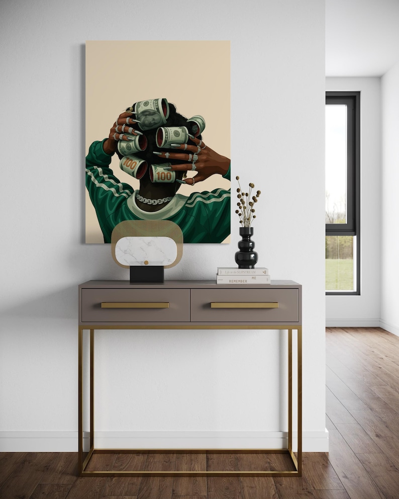 May include: A framed artwork depicts a person with dollar bills rolled into curlers. The person wears a green and white striped shirt and a silver chain. A gray console table with gold legs and a marble lamp are in front of the artwork.