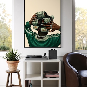 May include: A framed art print featuring a person with dollar bills styled as hair rollers. The person wears a green and white track jacket and multiple rings. The artwork is displayed in a living room setting.