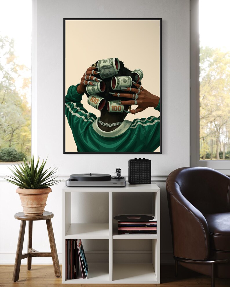 May include: A framed art print featuring a person with dollar bills styled as hair rollers. The person wears a green and white track jacket and multiple rings. The artwork is displayed in a living room setting.