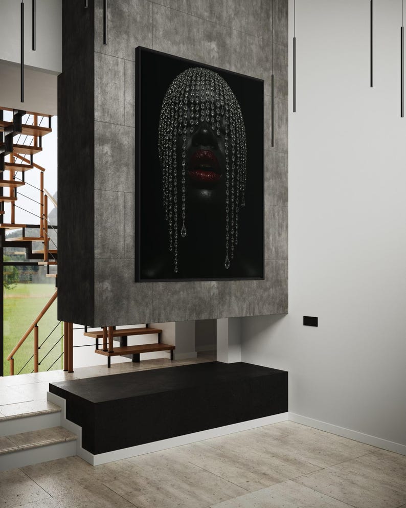 Pode incluir: Uma obra de arte emoldurada com um retrato de uma pessoa com pele escura, adornada com um adorno de cabe&ccedil;a de cristal e l&aacute;bios vermelhos. A obra de arte &eacute; montada em uma estrutura de concreto cinza escuro, com um banco preto abaixo. O ambiente interno inclui uma escada e ilumina&ccedil;&atilde;o moderna.