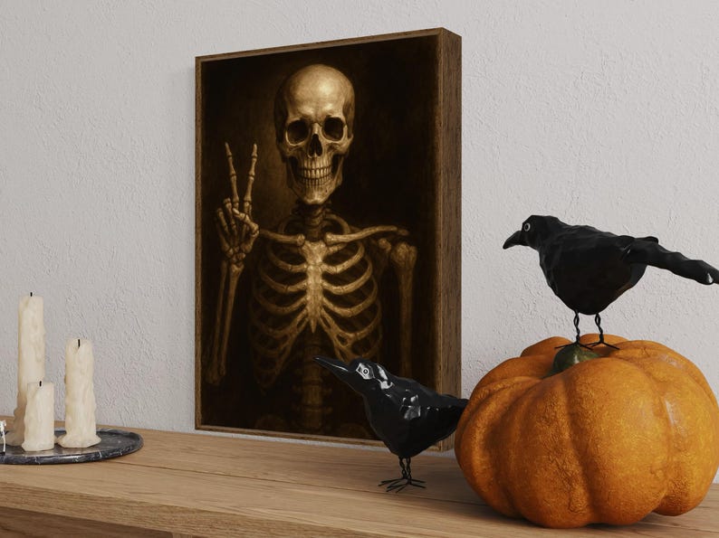 Puede incluir: Una obra de arte enmarcada representa un esqueleto dorado haciendo el signo de la paz. Dos figuras de cuervos negros y una calabaza naranja se encuentran sobre una superficie de madera. Tres velas blancas est&aacute;n en una bandeja plateada. Decoraci&oacute;n de Halloween.