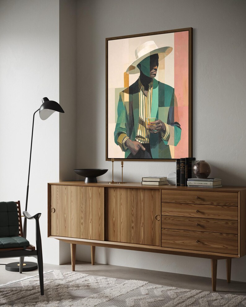 May include: A framed art print depicts a person in a white hat and green blazer holding a glass. The artwork hangs above a wooden sideboard with sliding doors and drawers. A black lamp and chair are in the foreground.