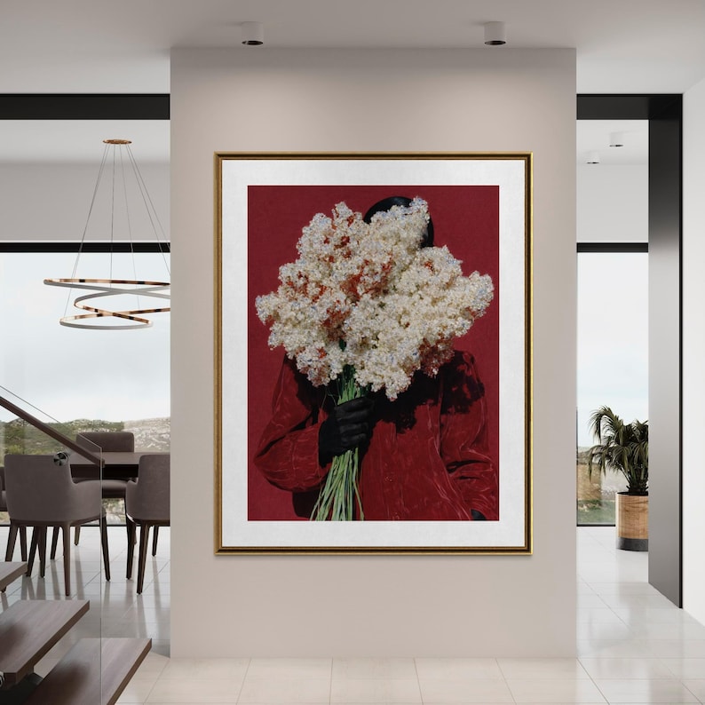May include: A framed art print featuring a person holding a large bouquet of white and brown flowers against a red background. The person is wearing a red jacket and black gloves. The artwork is displayed in a modern interior setting.
