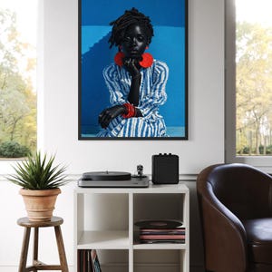 May include: A framed portrait of a person with dark skin, wearing a blue and white striped dress and red jewellery. The portrait hangs above a white cube shelf with a record player, speaker, and vinyl records. A potted plant sits on a wooden stool.